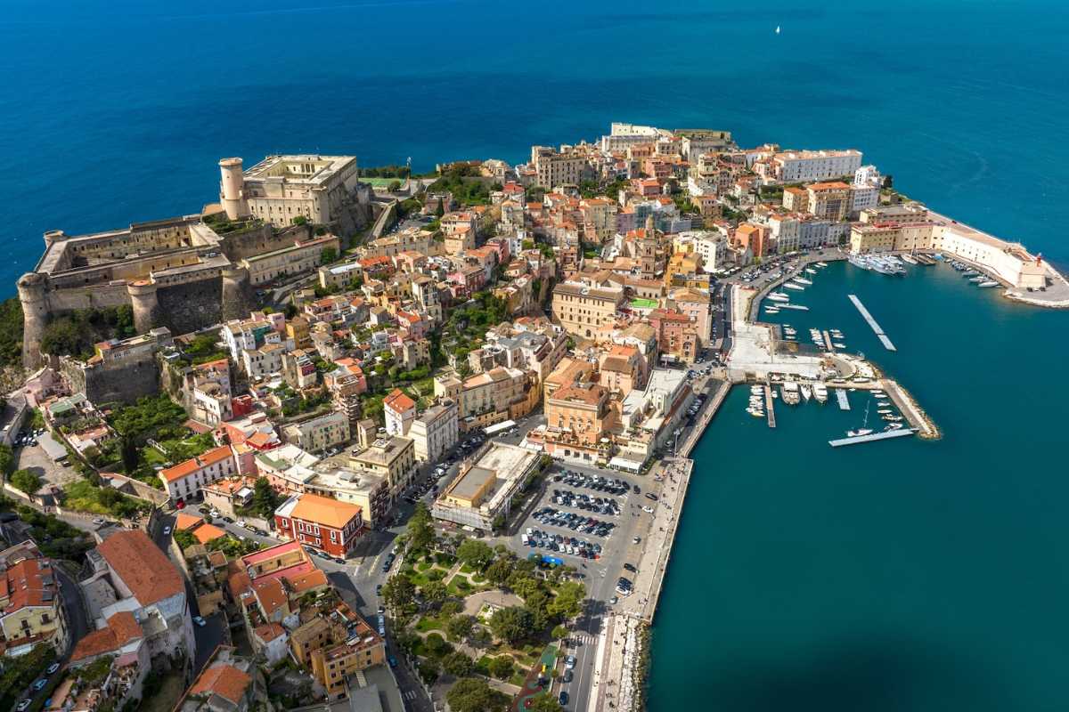 Scorcio pittoresco del borgo medievale di Gaeta: vicoli in pietra, balconi fioriti, vista sul mare e sul campanile romanico. Luce calda del pomeriggio.